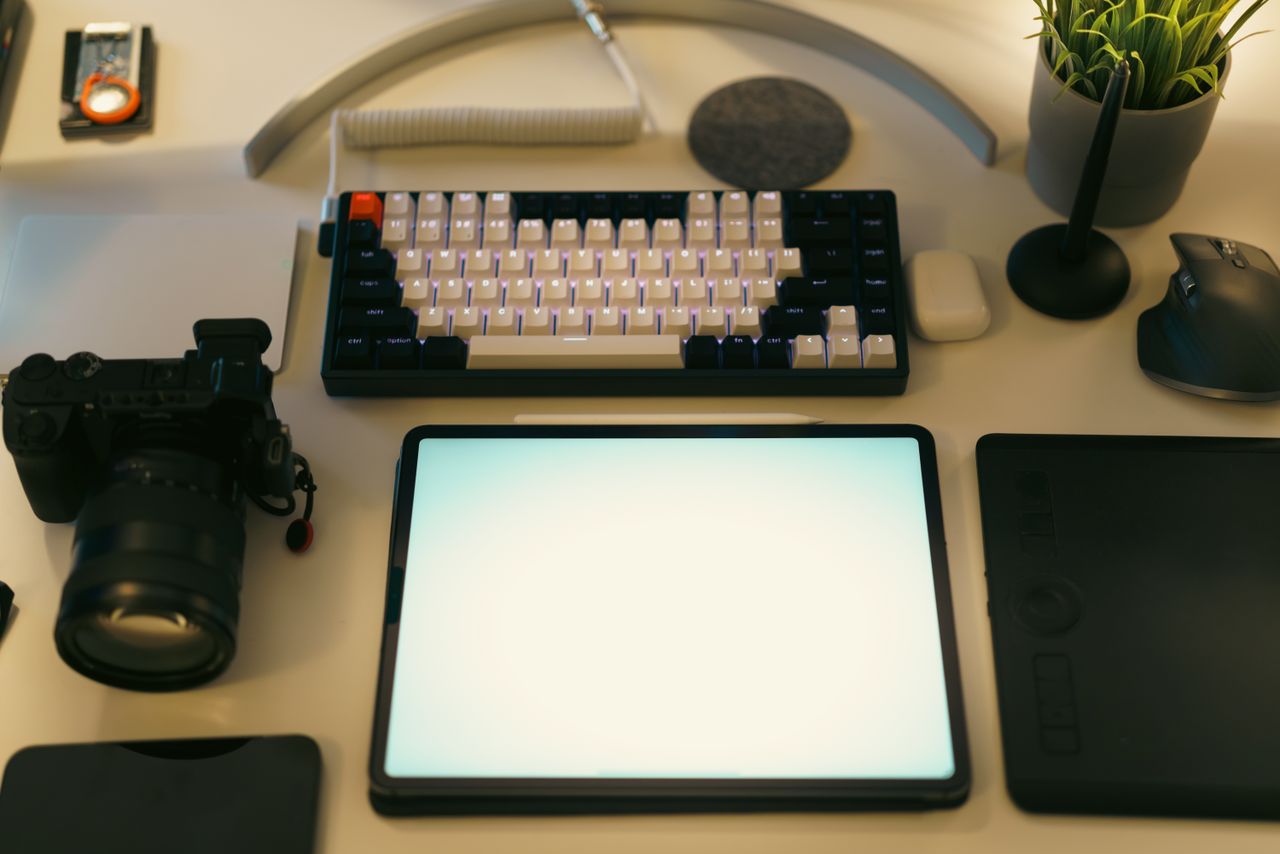 gallery-03 A stylish desk setup featuring a digital tablet, keyboard, camera, and plant, ideal for creative work.